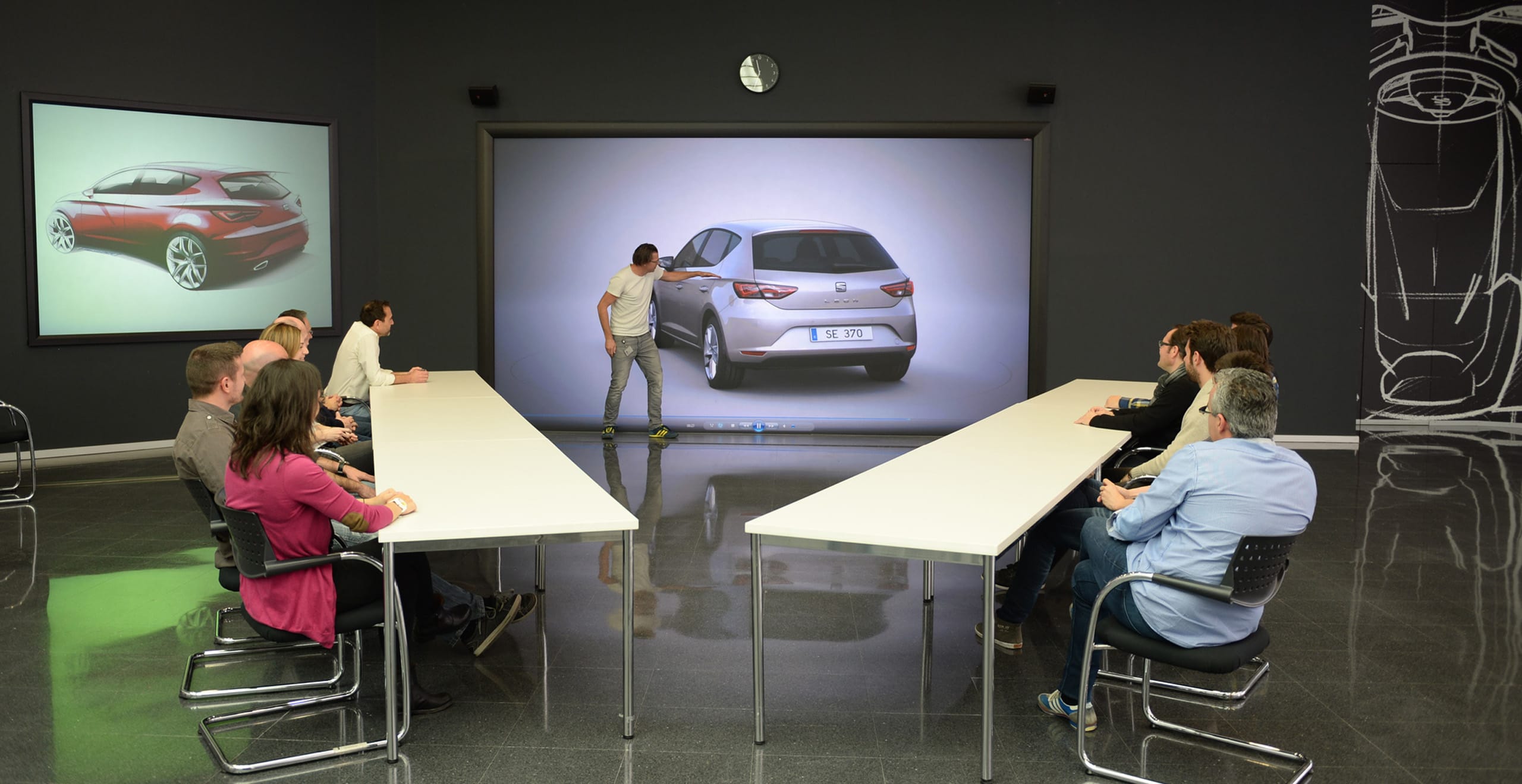Diskussion en man pekar på en bilmodell SEAT Leon med en grupp människor som sitter vid ett bord – SEAT Human Resources