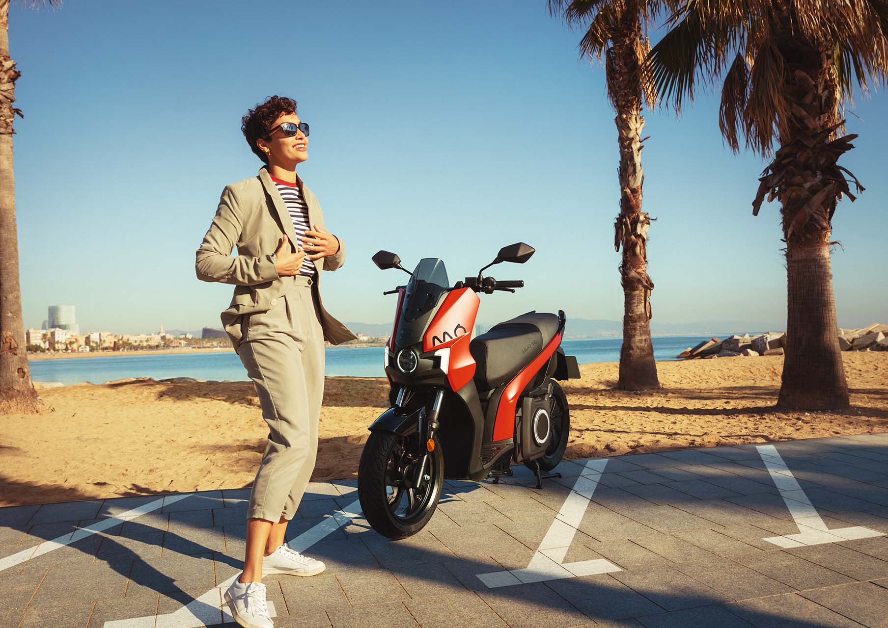 man standing at his SEAT MÓ 125 electric scooter parked at the beach