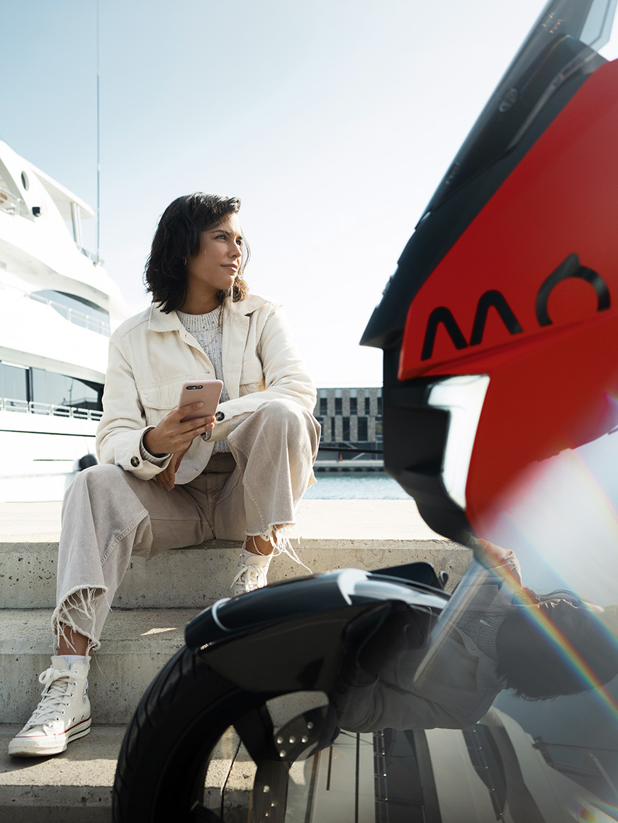 kvinna sitter vid sin parkerade elsparkcykel SEAT MÓ 125 i hamnen