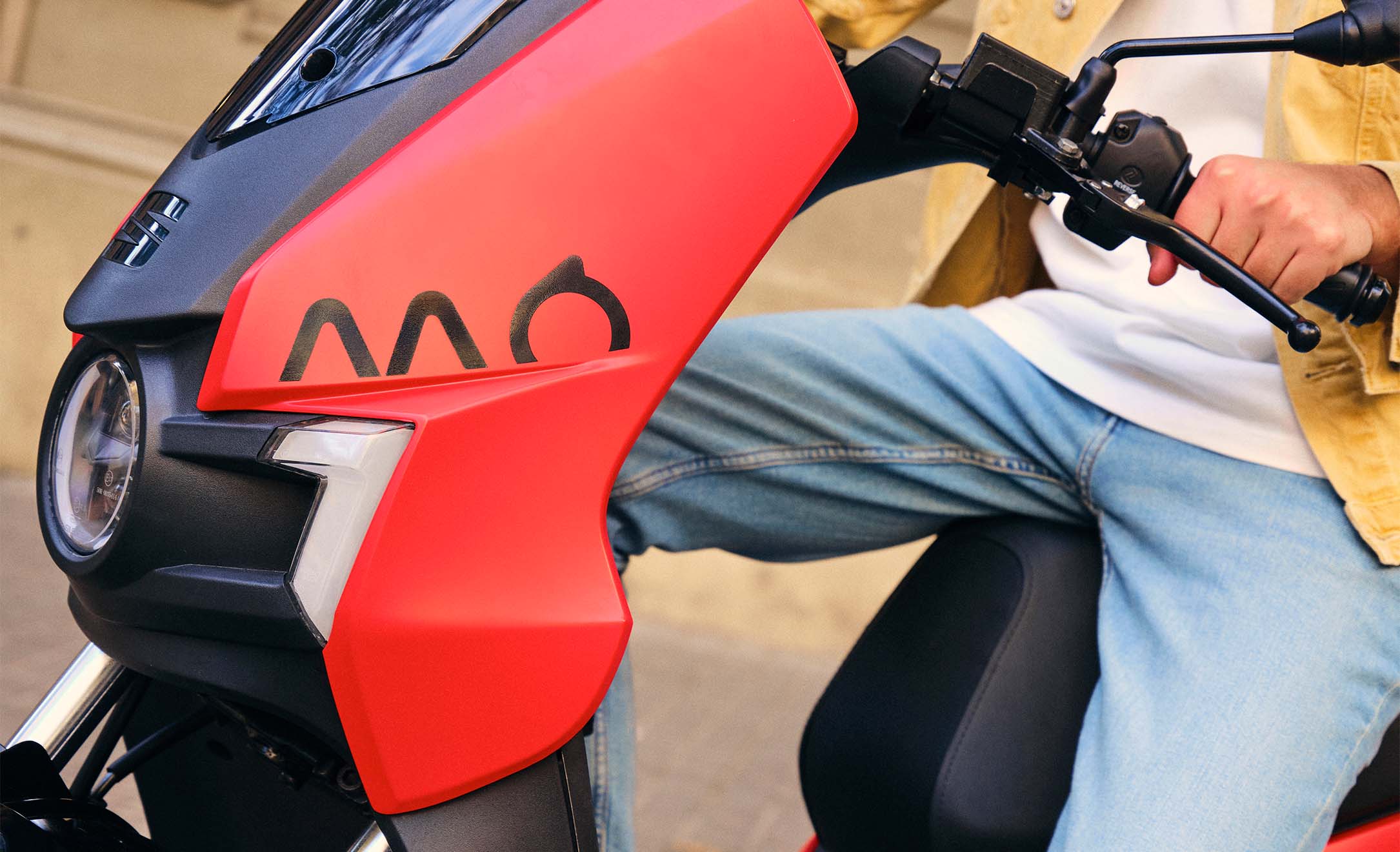 Närbild av en seat mo 125 som visar modellens röda färg, elscooterns eleganta designdetaljer och seat mo-logotypen. Den körs av en person klädd i jeans.