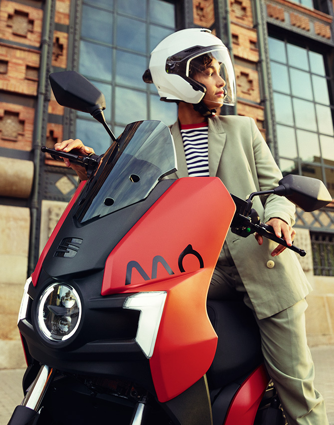 person wearing a helmet riding their SEAT MÓ 125 electric scooter by the coast