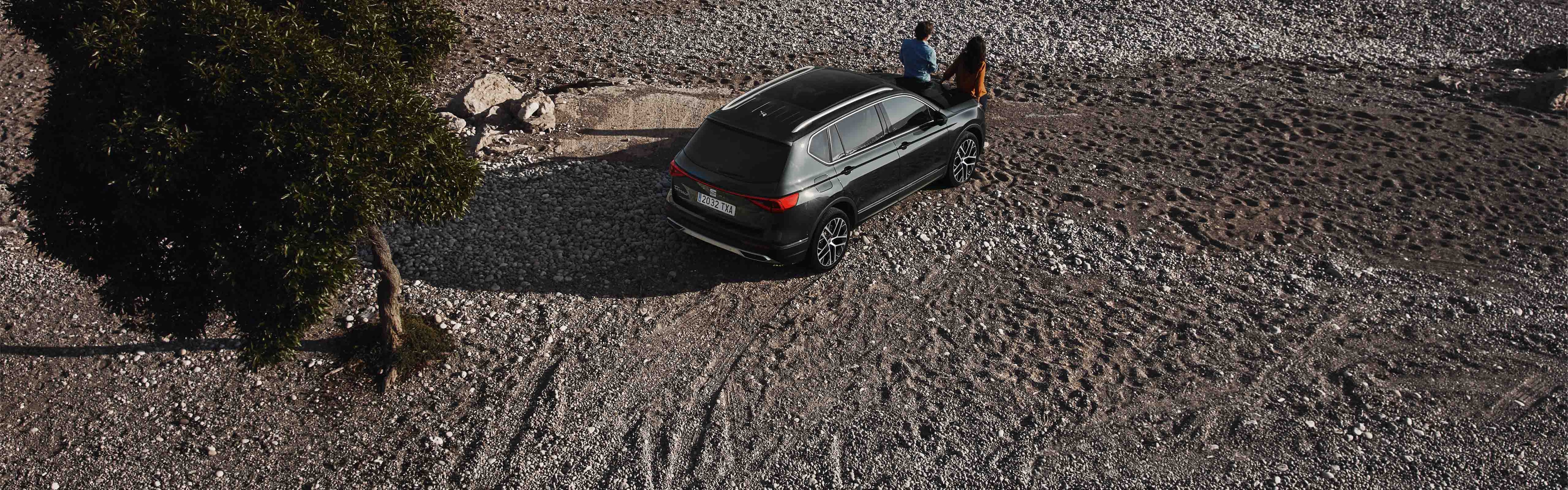 Couple sitting on the SEAT Tarraco XPERIENCE Dark Camouflage colour parked at the beach 